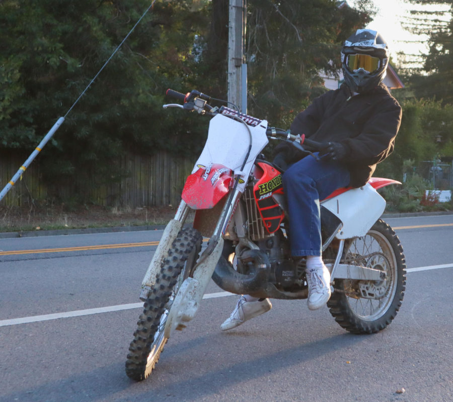 Maddock leans to the side, on the shoulder of the road while sitting on his dirt bike.