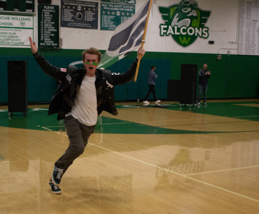Senior Class President Jack Long runs into the gym with an Archie Williams flag as students cheer for him from the bleachers.